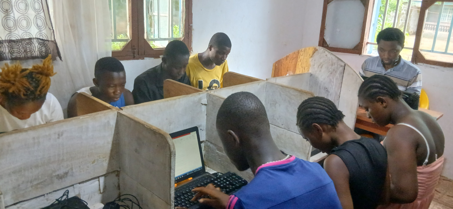 Young women and men working at laptops in wooden study booths during a Microsoft Word practical